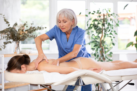 Experienced older professional masseuse doing back massage to young womanの写真素材