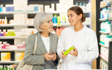 Modern pharmacy - pharmacist advising an mature woman when buying medicinal ointmentの写真素材