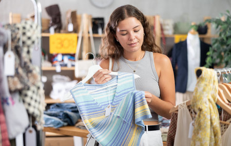 Young woman chooses a set of clothes for the summer. Visitor to the boutique examines new summer...