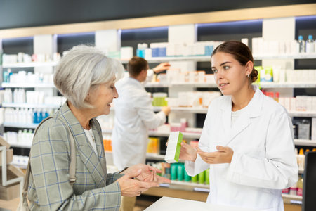 Girl apothecary hold package with cream and talks with senior woman client about nuances of careの写真素材