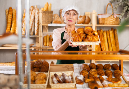 Positive elderly female seller offers to buy fresh croissantsの写真素材