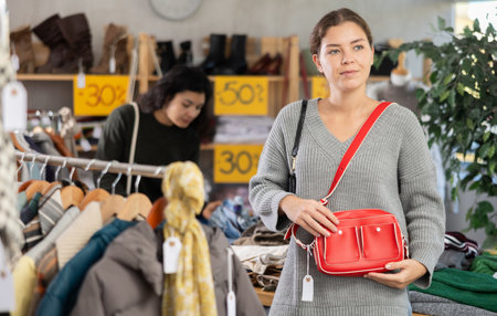 Girl is busy looking at clothes items in store, she chooses handbagの写真素材