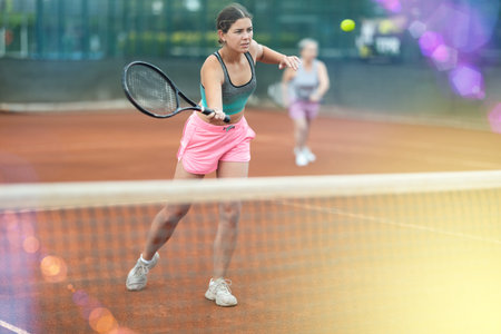 Girl swinging racket during doubles tennis match on outdoor courtの写真素材