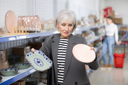 Smiling elderly woman choosing ceramic Asian style plates in storeの写真素材