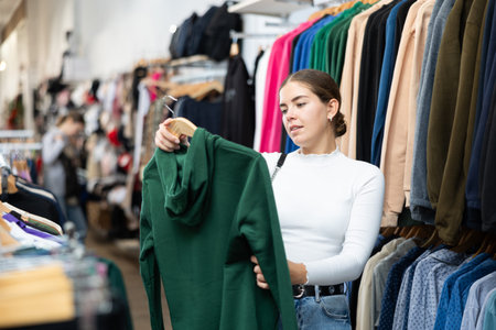 Young woman choosing sweatshirt in store