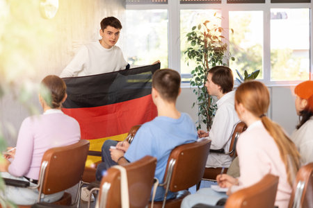 Young man tells his classmates the history of the state of Germany, holding national flag of Germany in his handsの写真素材