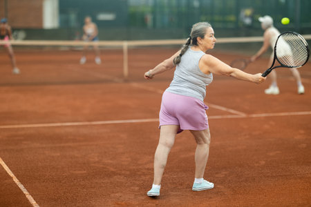 Two elderly women playing tennis against young womenの写真素材