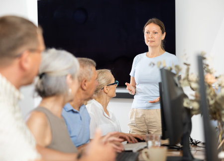 Mature people listen attentively to female teacher during computer teaching lesson in nursing home