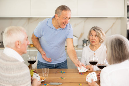 Cheerful friendly company of men and women sitting at kitchen table and enjoying the poker game....
