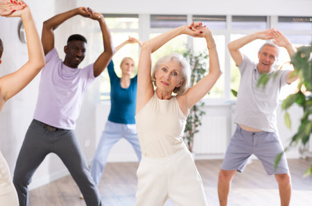 Active mature men and women practicing Jazz-funk dance in training hallの写真素材