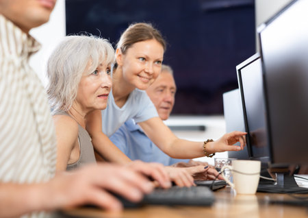Young female mentor explaining something to elderly woman at computer lessonの写真素材