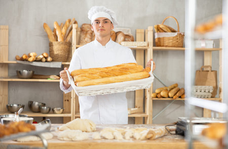 Young male baker holding baguettes in wicker basket