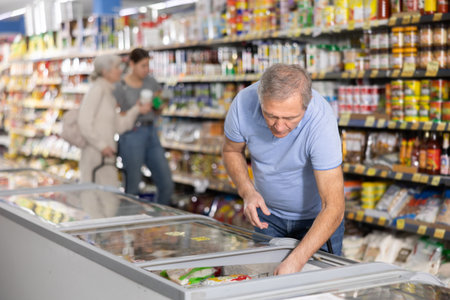 Mature man shopping in supermarket, choosing frozen convenience foodの写真素材