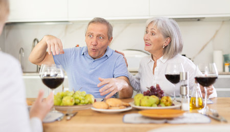 Mature married couple with female friend are sitting at table, enjoying food and wine, chatting.の写真素材