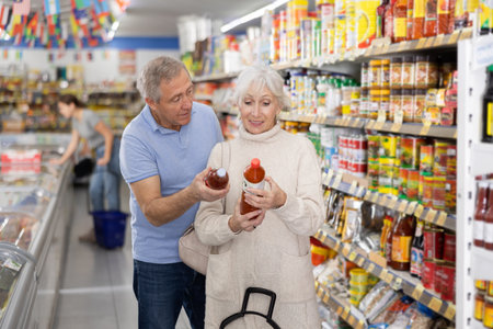Senior couple examining labels of sauces in grocery storeの写真素材