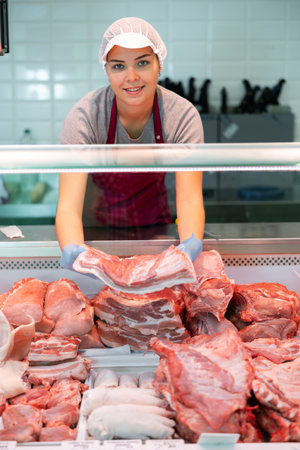 Young farmer woman in butcher shop takes raw pork ribs out of refrigeratorの写真素材