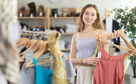 Woman chooses a set of clothes for the summer. Visitor to boutique examines the new summer collection of clothesの写真素材