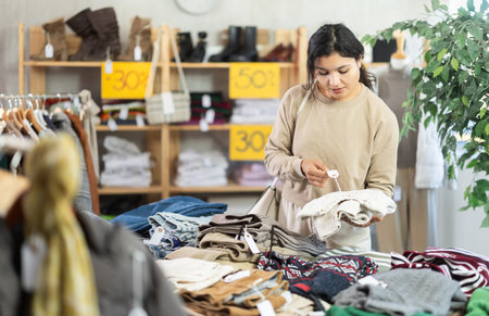 Latin girl is busy looking at clothes items in store, choose sweaterの写真素材