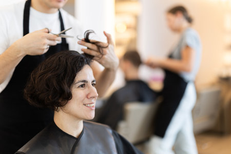 Young man barbershop employee stands next to female client, discussing details of haircutの写真素材