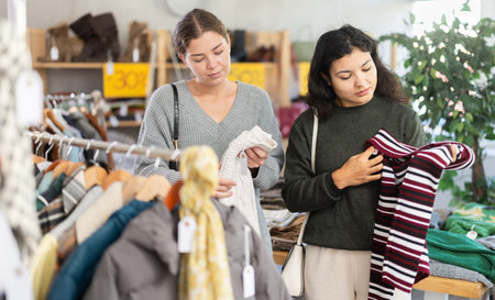 Latin woman with female companion is busy looking at clothes items, choose winter sweaterの写真素材