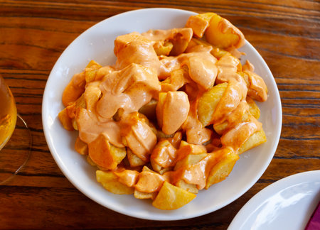 Spanish fried potatoes Patatas bravas served with cheese sauce and spicy sauce with paprika and chiliの写真素材