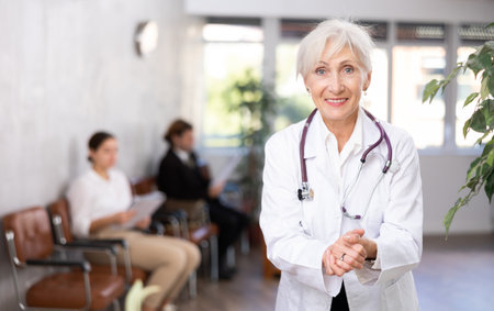 smiling mature medical female receptionist affably waiting for patients of clinic in waiting roomの写真素材