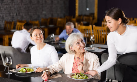 Smiling waitress fulfills order of young girl and elderly woman of restaurant visitors.の写真素材