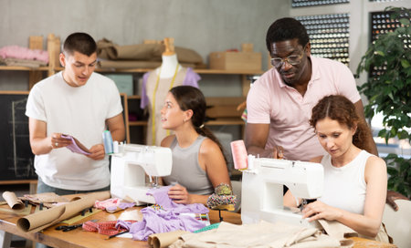 During lesson, man teacher helps student sew, others work with fabric, blank, dress patternsの写真素材