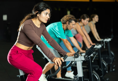 Sportive Latina girl doing spin bike exercises in well-equipped gymの写真素材