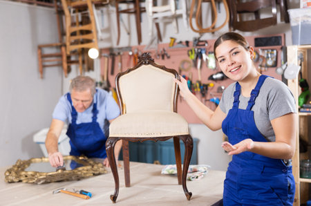 Girl restoration worker dressed in overalls poses in working atmosphere of workshopの写真素材