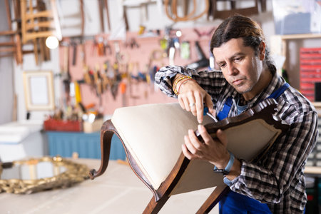 Male furniture maker working on vintage chair in workshopの写真素材