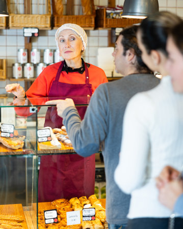 People place order at bakery, buy sweet pastries, senior woman worker serving peopleの写真素材