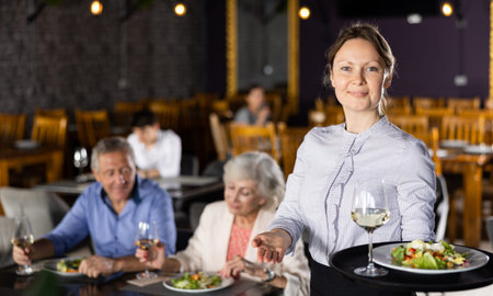 Hospitable waitress with serving tray meeting guests in restaurant