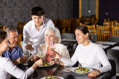 Elderly couple and young couple and adult woman having dinner in restaurantの写真素材