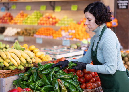 Adult woman seller puts bell peppers on displayの写真素材