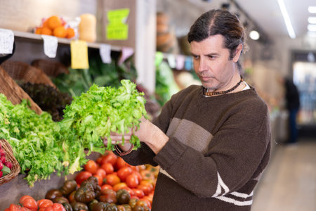 Adult man choosing lettuce in vegetable shopの写真素材