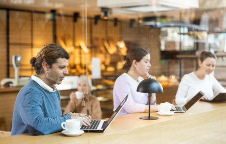 Focused man browsing websites on laptop and drinking coffee in cafeの写真素材
