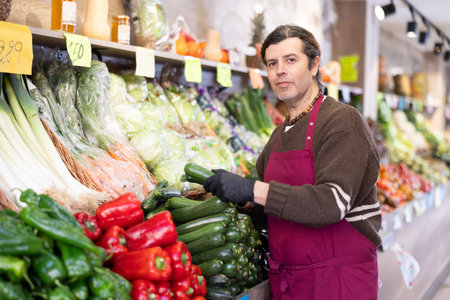 Adult man seller puts zucchini on displayの写真素材
