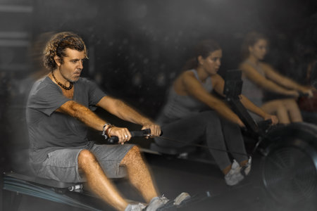 Diligent middle-aged man training with rowing machine in sports hallの写真素材