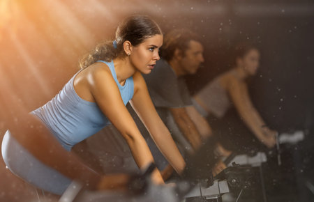 Sportive young girl doing spin bike exercises in well-equipped gym