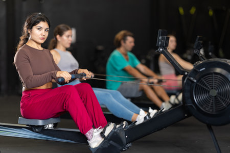 Sportive Latina girl training with rowing machine in sports hallの写真素材