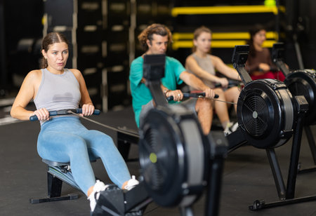 Sportive young girl training with rowing machine in sports hallの写真素材