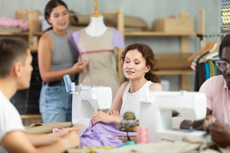 Positive woman working at machine during group sewing course for adultsの写真素材