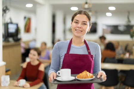 Young woman waiter with tray of coffee and croissantの写真素材