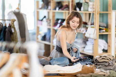 Positive young girl choosing jeans pantaloons in clothing store