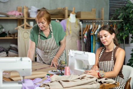 Mature dressmaker drawing patterns next to young assistantの写真素材