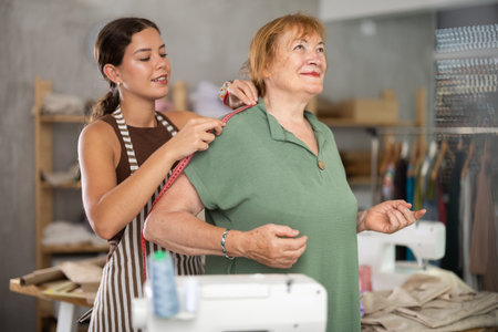 Young seamstress takes measurements from mature womanの写真素材