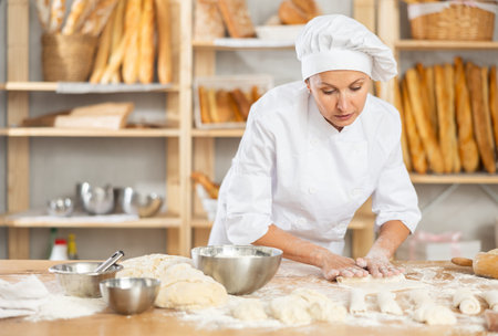 Female baker preparing croissant dough - kneading, rolling and cutting dough on table in bakery