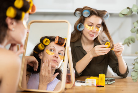 Two women curl their hair with curlers and use patchesの写真素材
