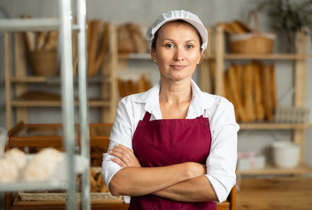 Woman baker in white coat overall and cap stands in trading hall of bakery